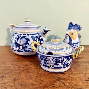 May include: A ceramic tea set featuring a teapot, a lidded sugar bowl with two yellow twisted handles, and a rooster-shaped creamer. Each piece is decorated with intricate blue and white floral scrollwork patterns and yellow accents.