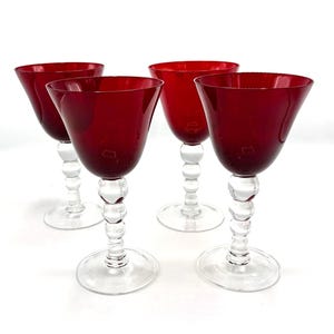 May include: Four ruby red wine glasses with clear, beaded stems and round bases. The glasses have a classic, elegant design, perfect for serving wine at a dinner party or special occasion.