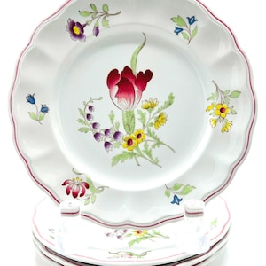May include: A stack of white ceramic salad plates with scalloped edges and a thin red rim. The center of the top plate features a large red tulip surrounded by smaller yellow, purple, and blue floral motifs. The word Salad is printed at the top.