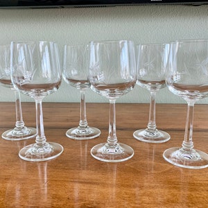 May include: Set of six clear glass wine glasses with etched designs. The glasses have a round bowl and a long stem.