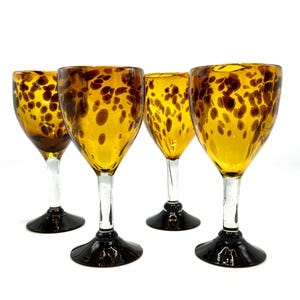 May include: Four amber-colored wine glasses with a speckled pattern. The glasses have clear stems and black bases. The glasses are arranged on a white background.