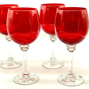 May include: A set of four wine glasses featuring deep red bowls and clear glass stems and bases. Each glass has a rounded bowl shape, a slender stem with a decorative knob detail near the top, and a circular foot for stability on flat surfaces.