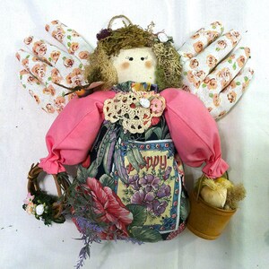 May include: A handmade fabric angel doll with pink clothing, a floral print skirt, and gardening gloves for wings. The doll is holding a small wicker basket with a flower wreath and a small bucket with a single onion.