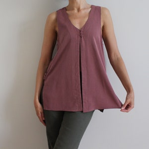 May include: A mauve sleeveless top with a V-neckline and a single button closure at the center front. The top has a long, flowing silhouette and a slightly flared hem.