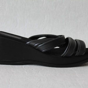 May include: Black leather wedge sandals with multiple straps across the foot.