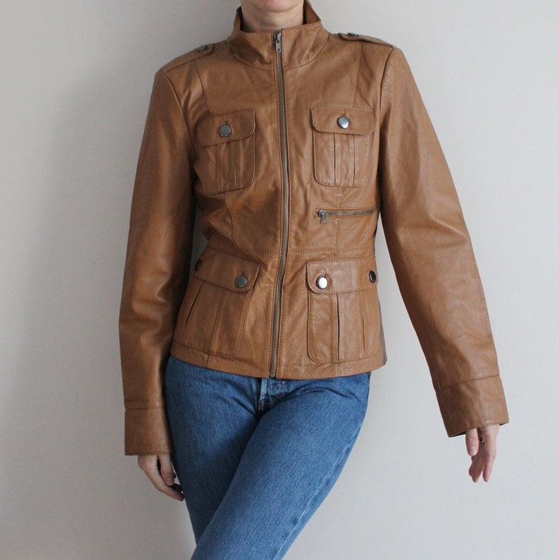 May include: A brown leather jacket with a zipper closure and multiple pockets. The jacket has a stand-up collar and long sleeves.