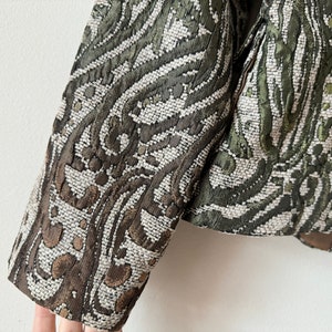 K&ouml;nnte beinhalten: Ein gr&uuml;ner und brauner gemusterter Blazer mit gewebter Textur. Der Blazer hat eine figurbetonte Silhouette und lange &Auml;rmel.
