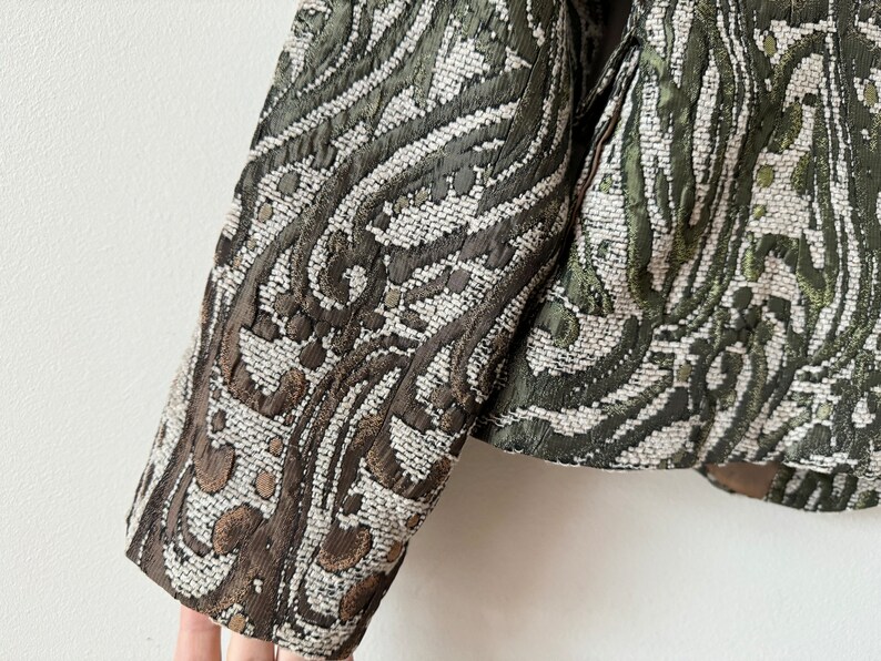 K&ouml;nnte beinhalten: Ein gr&uuml;ner und brauner gemusterter Blazer mit gewebter Textur. Der Blazer hat eine figurbetonte Silhouette und lange &Auml;rmel.