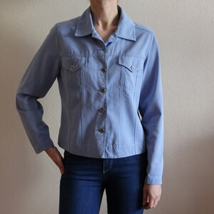 Könnte beinhalten: Eine hellblaue Jeansjacke mit Knopfleiste und zwei Pattentaschen. Die Jacke hat einen klassischen Stil und ist aus einem weichen, bequemen Stoff gefertigt.
