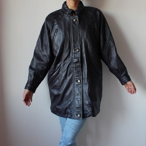 May include: A black leather jacket with a button-up front and multiple pockets. The jacket has a long, oversized fit.