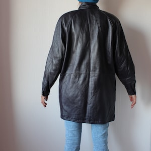 May include: A long black leather jacket with a geometric design on the back. The jacket has a collar and long sleeves.