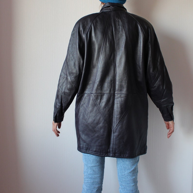 May include: A long black leather jacket with a geometric design on the back. The jacket has a collar and long sleeves.