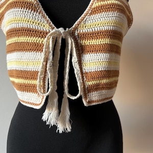 Puede incluir: Un top de crochet con un frente de corbata y borlas. El top est&aacute; rayado en marr&oacute;n, blanco y amarillo.