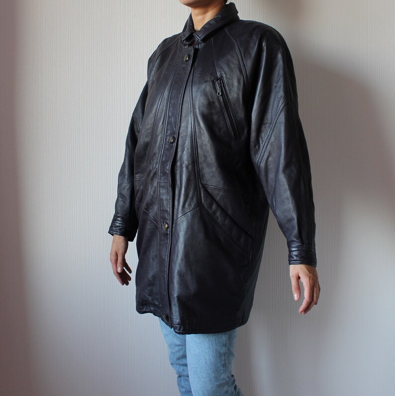 May include: A long black leather jacket with a button-up front and a collar. The jacket has a slightly oversized fit and features a variety of pockets and seams.