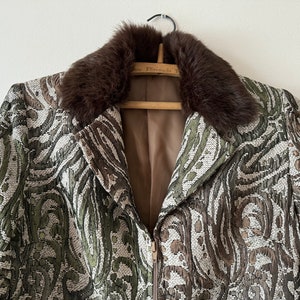 K&ouml;nnte beinhalten: Eine braune gemusterte Jacke mit einem braunen Pelzkragen. Die Jacke hat einen Rei&szlig;verschluss und ein braunes Futter.