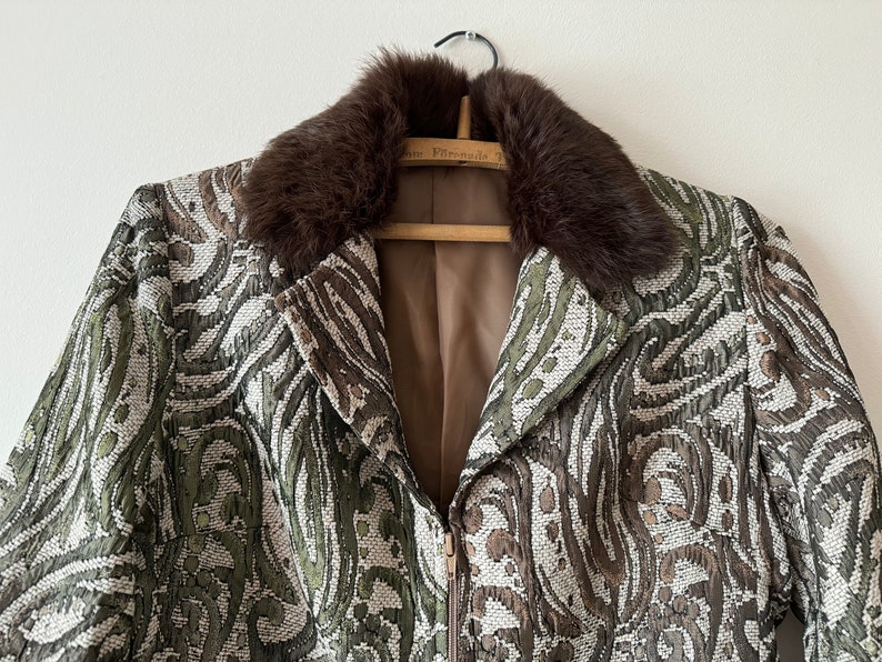 K&ouml;nnte beinhalten: Eine braune gemusterte Jacke mit einem braunen Pelzkragen. Die Jacke hat einen Rei&szlig;verschluss und ein braunes Futter.