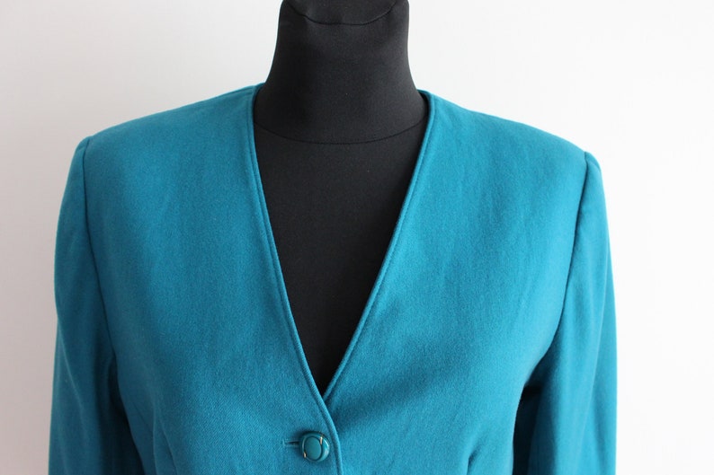 May include: A teal blue blazer with a single button fastening and a v-neck.