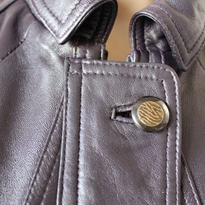 May include: Close-up of a purple leather jacket with a zipper and a button with a zebra print design.
