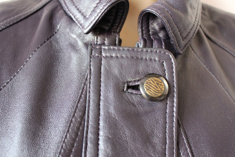 May include: Close-up of a purple leather jacket with a zipper and a button with a zebra print design.
