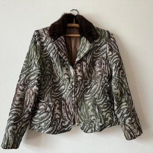 K&ouml;nnte beinhalten: Eine braune und gr&uuml;ne gemusterte Jacke mit einem braunen Pelzkragen. Die Jacke hat einen Rei&szlig;verschluss und lange &Auml;rmel.