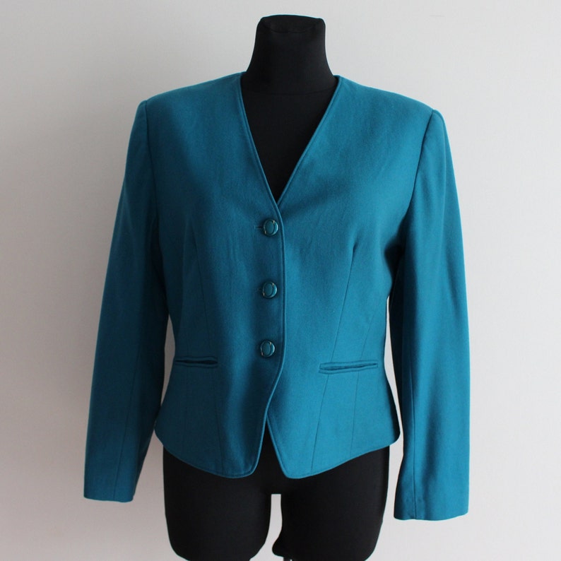 May include: A teal blazer with a v-neck and four buttons. The blazer has a fitted silhouette and long sleeves.