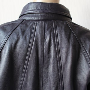 May include: A dark purple leather jacket with a collared neckline and a button closure. The jacket has a seam down the center of the back and seams on the shoulders.
