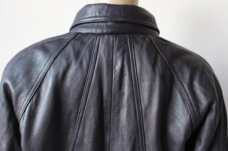 May include: A dark purple leather jacket with a collared neckline and a button closure. The jacket has a seam down the center of the back and seams on the shoulders.