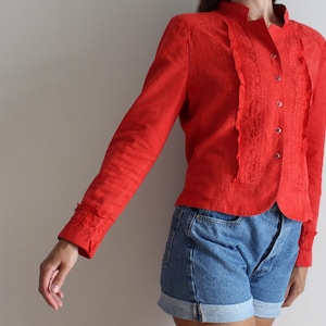 May include: A red long-sleeved blouse with a ruffled front and button closure.