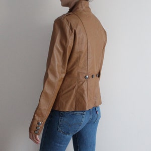 May include: A brown leather jacket with a stand-up collar and button closures. The jacket has a fitted silhouette and a slightly cropped length.