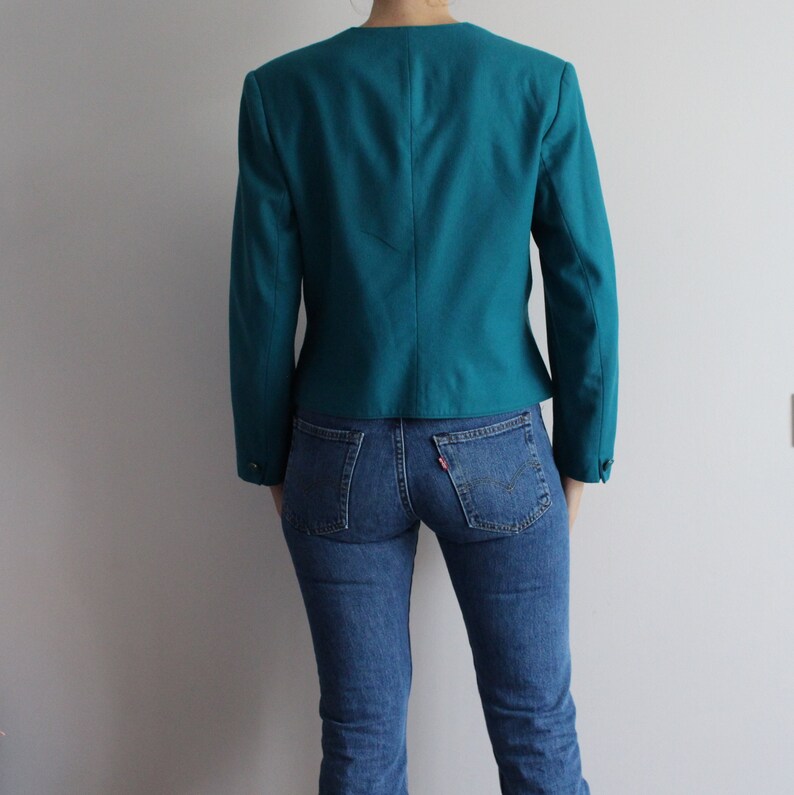 May include: A teal blazer with long sleeves and a fitted silhouette. The blazer is made of a smooth, textured fabric.