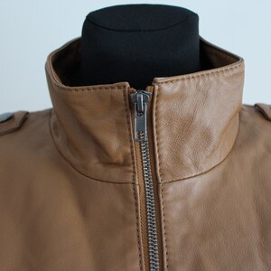May include: A brown leather jacket with a zipper closure and a high collar.