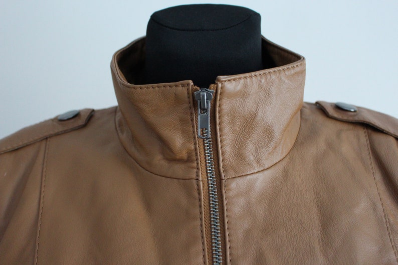 May include: A brown leather jacket with a zipper closure and a high collar.