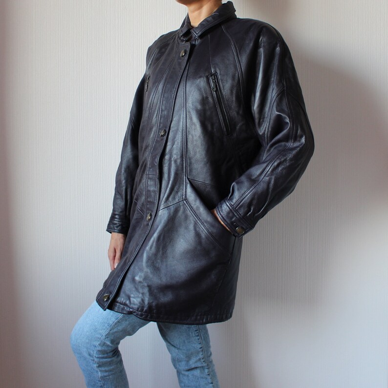 May include: A long, dark blue leather jacket with a button-up front, two zippered pockets, and a collar. The jacket has a relaxed fit and is made of a soft, supple leather.
