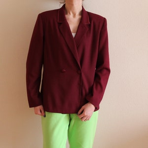 Könnte beinhalten: Ein burgunderfarbener Blazer mit doppelreihigem Verschluss und einem einzigen Knopf. Der Blazer hat einen Schalkragen und lange Ärmel.