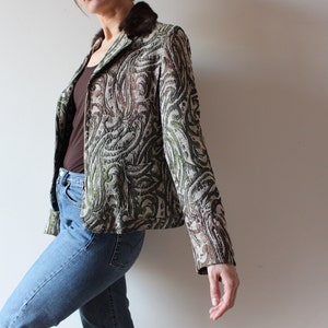 K&ouml;nnte beinhalten: Ein gr&uuml;ner, brauner und wei&szlig;er gemusterter Blazer mit einem braunen Pelzkragen. Der Blazer ist kurz und hat eine figurbetonte Silhouette.