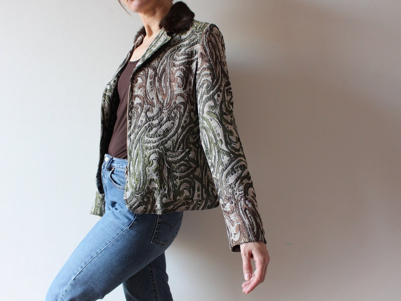 K&ouml;nnte beinhalten: Ein gr&uuml;ner, brauner und wei&szlig;er gemusterter Blazer mit einem braunen Pelzkragen. Der Blazer ist kurz und hat eine figurbetonte Silhouette.