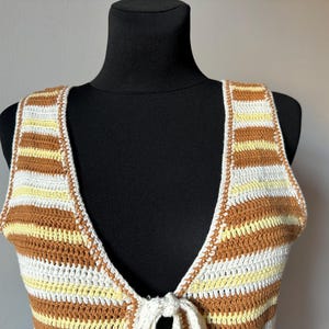 Puede incluir: Un top de crochet a rayas marrones y blancas con un lazo en el escote.