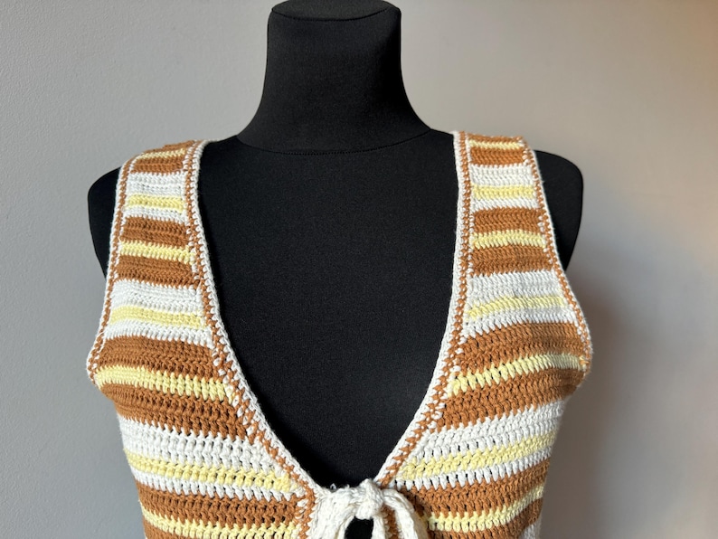 Puede incluir: Un top de crochet a rayas marrones y blancas con un lazo en el escote.