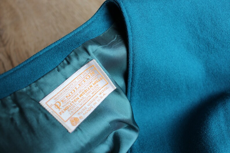May include: A teal blue Pendleton woolen mills label with white text that reads "warranted to give satisfaction Pendleton woolen mills Portland, Oregon 100% virgin wool pure virgin wool made in U.S.A."