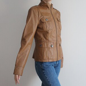 May include: A brown leather jacket with a zipper closure and multiple pockets. The jacket has a stand-up collar and long sleeves.