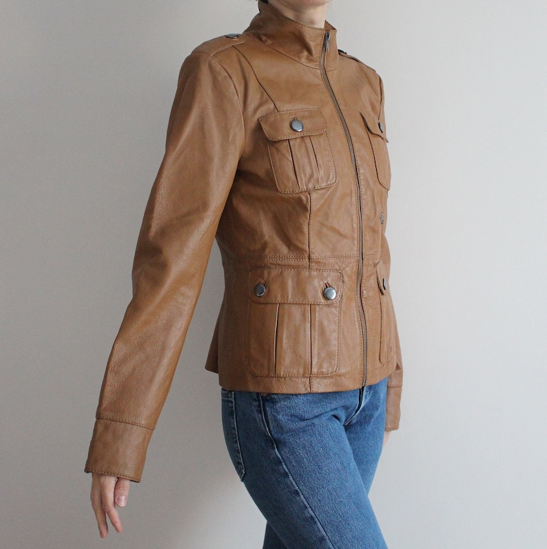 May include: A brown leather jacket with a zipper closure and multiple pockets. The jacket has a stand-up collar and long sleeves.