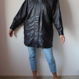 May include: A long black leather jacket with a button-up front and multiple pockets. The jacket has a slightly oversized fit and a relaxed silhouette.