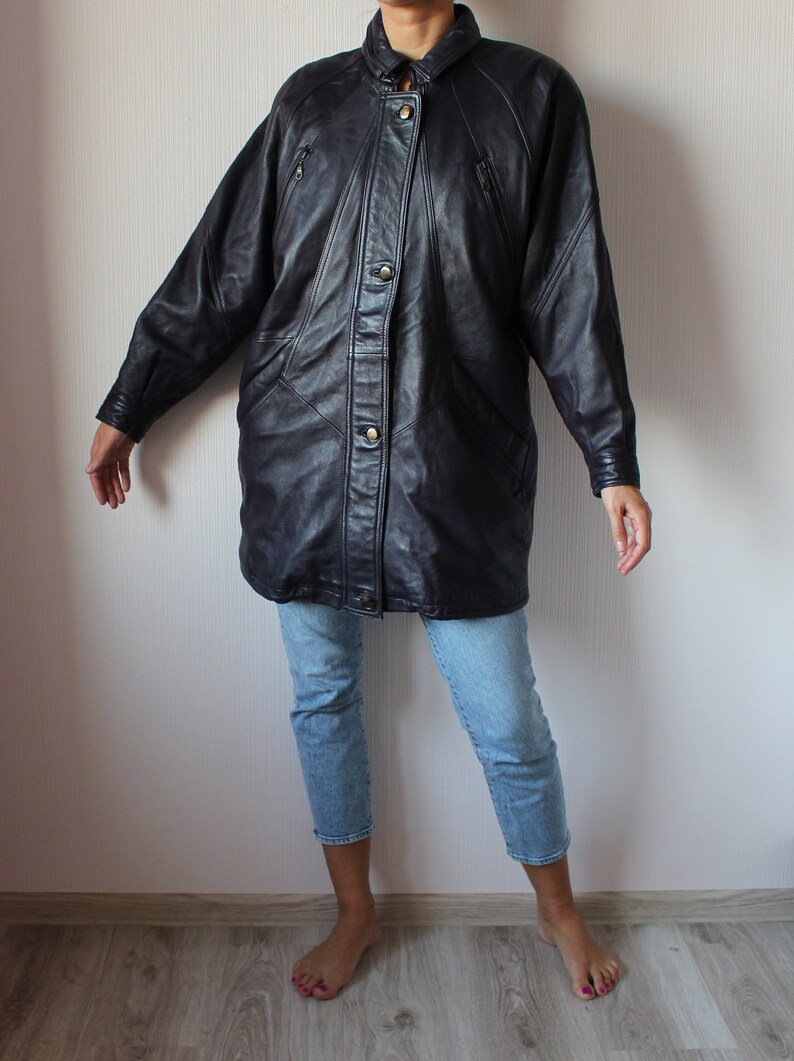 May include: A long black leather jacket with a button-up front and multiple pockets. The jacket has a slightly oversized fit and a relaxed silhouette.