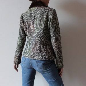 K&ouml;nnte beinhalten: Eine braune, gr&uuml;ne und wei&szlig;e gemusterte Jacke mit einem Kunstfellkragen. Die Jacke wird &uuml;ber einer blauen Jeans getragen.