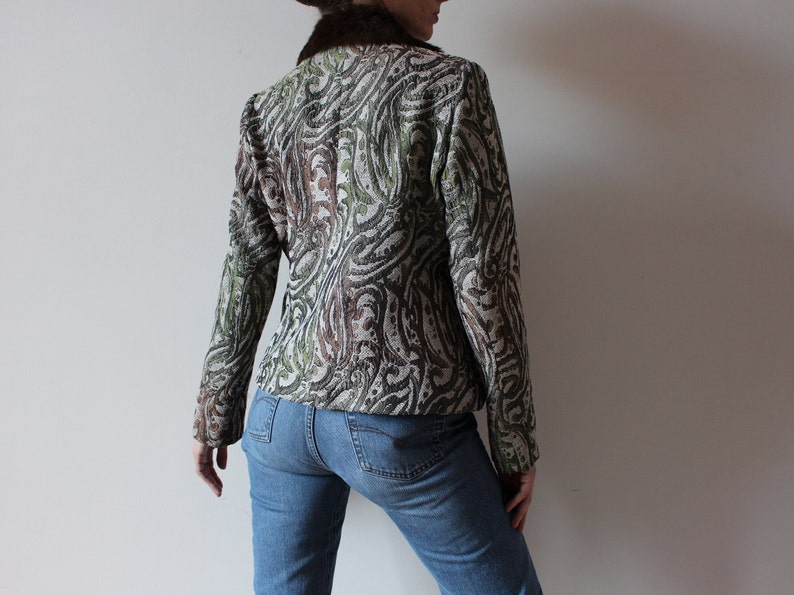 K&ouml;nnte beinhalten: Eine braune, gr&uuml;ne und wei&szlig;e gemusterte Jacke mit einem Kunstfellkragen. Die Jacke wird &uuml;ber einer blauen Jeans getragen.