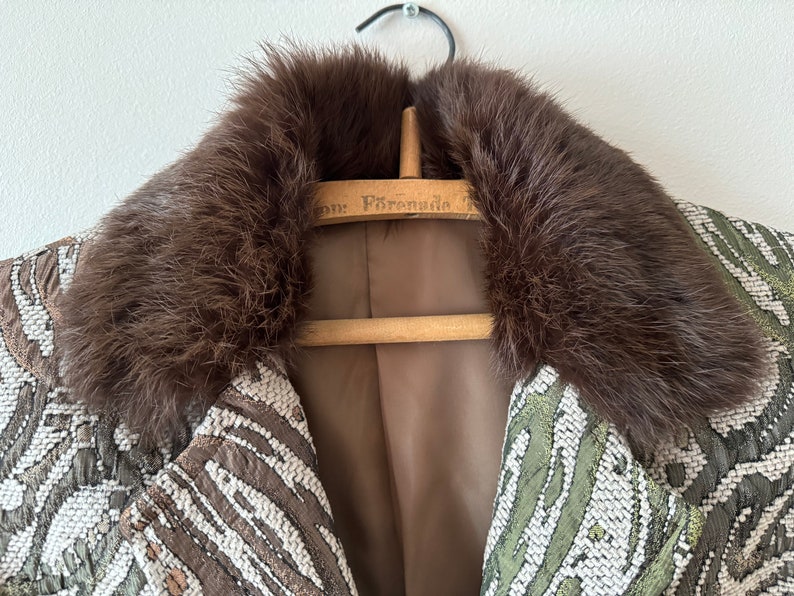 K&ouml;nnte beinhalten: Ein brauner Pelzkragen an einer Jacke mit gr&uuml;nem und wei&szlig;em Muster. Die Jacke h&auml;ngt an einem Holzb&uuml;gel mit dem aufgedruckten Text "For Presidio".