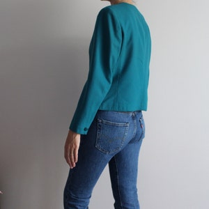 May include: A teal blazer with long sleeves and a button fastening. The blazer is cropped and has a fitted silhouette.