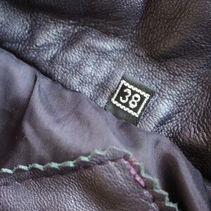 May include: Close-up of a dark purple leather jacket with a black size tag that says "38" on it.