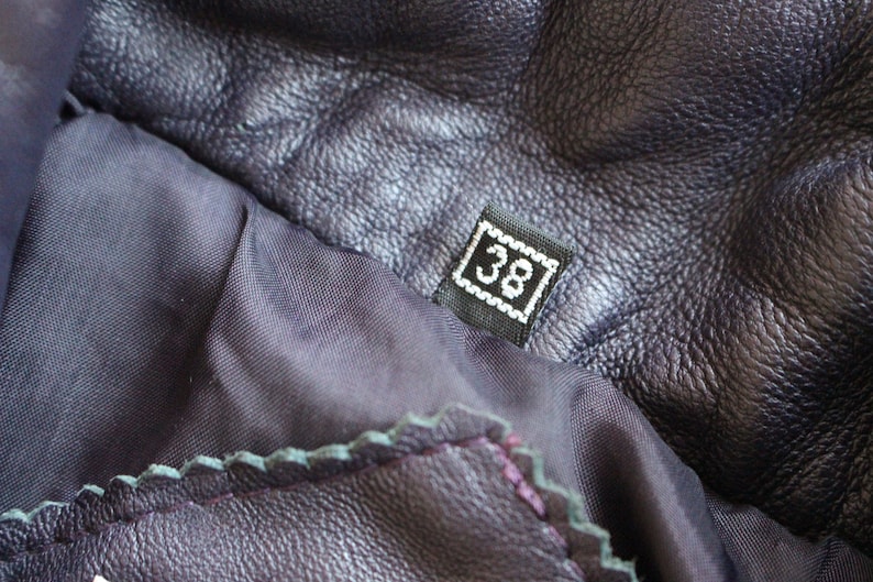 May include: Close-up of a dark purple leather jacket with a black size tag that says "38" on it.