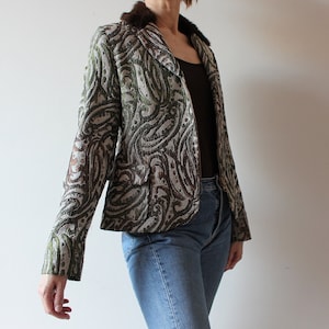K&ouml;nnte beinhalten: Ein brauner und gr&uuml;ner gemusterter Blazer mit einem Kunstfellkragen. Der Blazer hat eine figurbetonte Silhouette und einen einreihigen Verschluss.